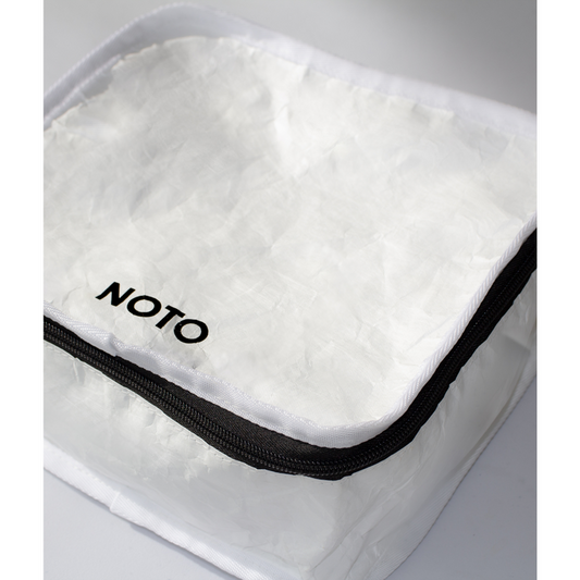 A white NOTO branded kit bag with a black zipper, made of Tyvek fabric. The bag is shown partially opened, displaying the brand name on the inside.